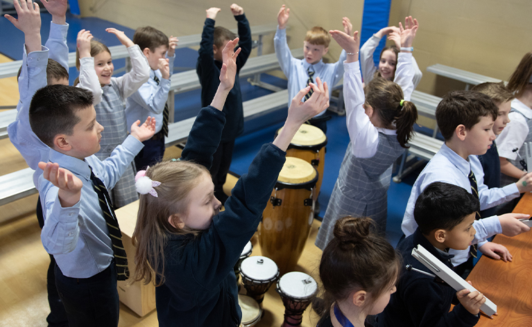 St. John drumming group students all putting their hands up above their heads